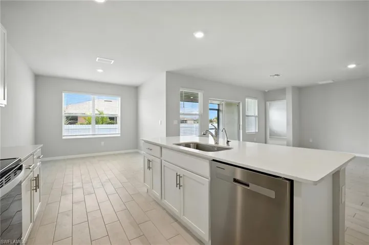 Kitchen island with integrated stainless steel sink and appliance, white cabinetry, and light-toned countertops