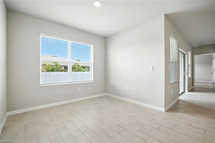 Spacious room with light gray walls, large window with horizontal blinds, recessed ceiling light, wood-finish tile flooring, and a glass sliding door