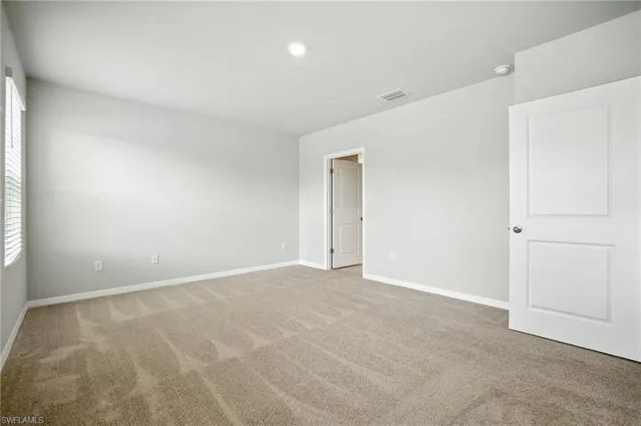 Spacious interior room with neutral-toned carpeting, white baseboards, and light gray wall paint