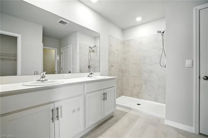 Bathroom featuring a double vanity with white cabinetry and chrome fixtures, a broad mirror, and a walk-in shower with tiled walls and a handheld showerhead
