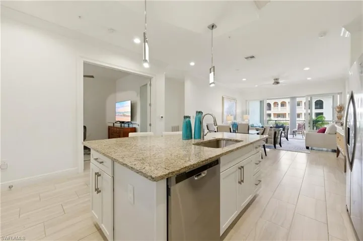 Kitchen featuring stainless steel appliances, white cabinets, an island with sink, ceiling fan, and light stone countertops