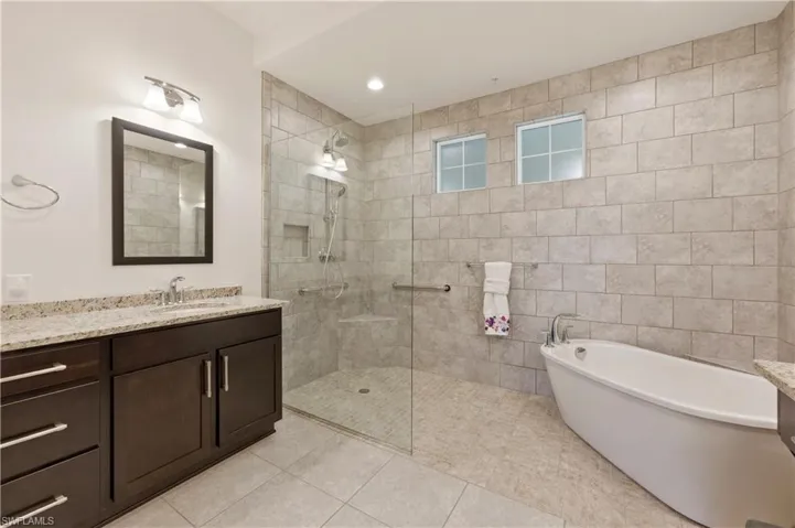 Full bath with vanity, a walk in shower, a freestanding bath, light tile patterned floors, and recessed lighting