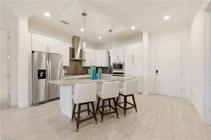 Kitchen featuring stainless steel appliances, a breakfast bar, white cabinets, a kitchen island with sink, and light stone countertops