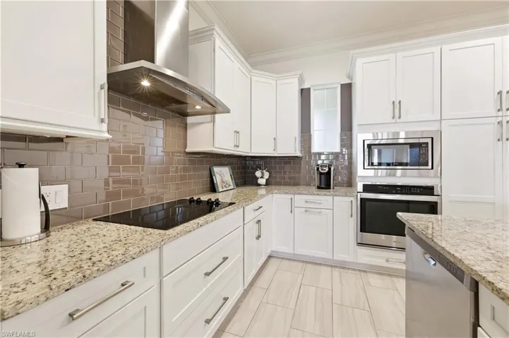 Kitchen featuring stainless steel appliances, white cabinetry, ornamental molding, backsplash, and light stone countertops