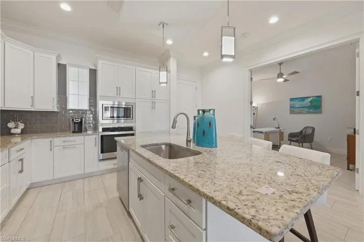 Kitchen with a kitchen bar, decorative backsplash, white cabinetry, stainless steel appliances, and light stone counters