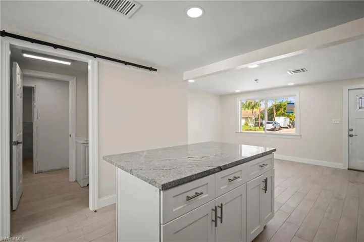 Kitchen with a barn door, light wood finished floors, a kitchen island, light stone countertops, and recessed lighting