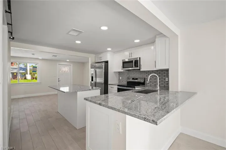 Kitchen with a center island, stainless steel appliances, light wood-style floors, decorative backsplash, and white cabinetry