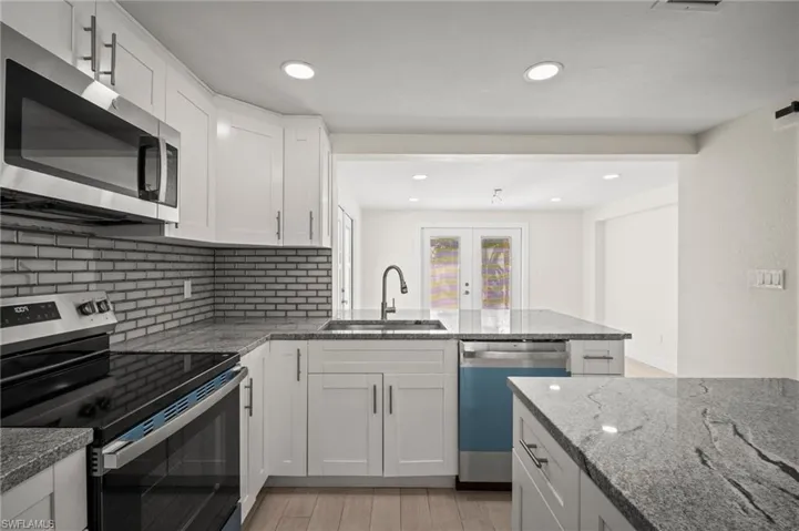 Kitchen with appliances with stainless steel finishes, decorative backsplash, white cabinetry, light stone countertops, and a peninsula