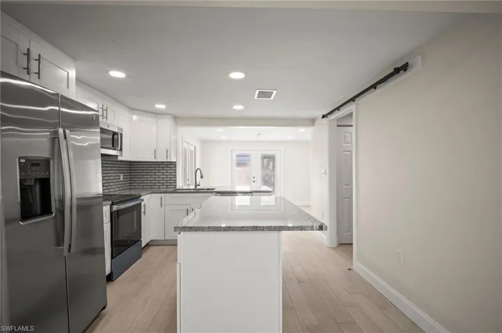 Kitchen featuring stainless steel appliances, a peninsula, white cabinetry, light wood-style flooring, and tasteful backsplash
