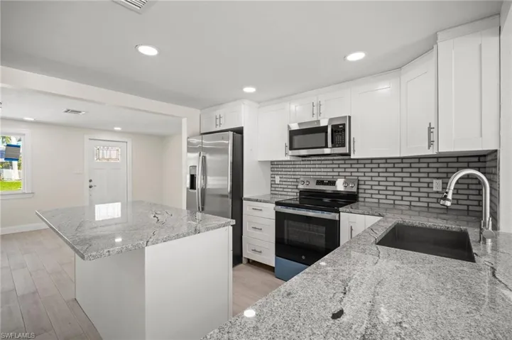 Kitchen with appliances with stainless steel finishes, a kitchen island, light stone countertops, tasteful backsplash, and white cabinetry