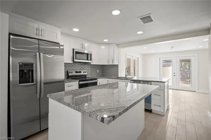 Kitchen with a peninsula, appliances with stainless steel finishes, a kitchen island, light wood-style floors, and recessed lighting