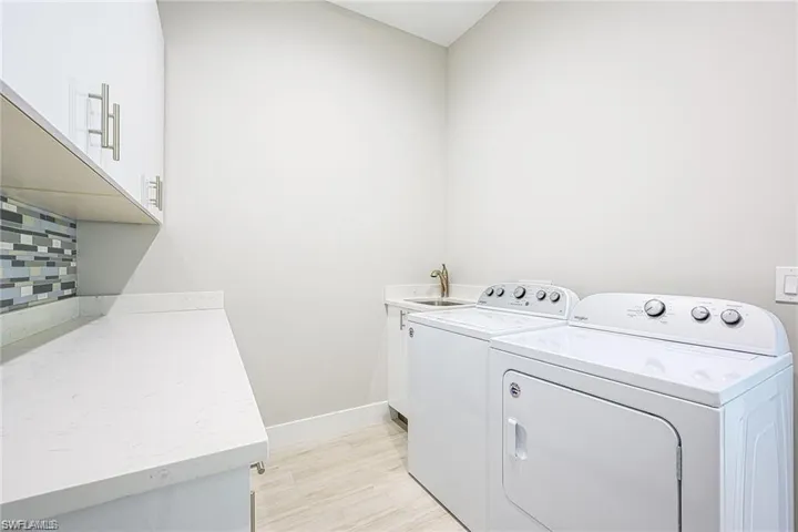 Laundry area featuring sink, washer and clothes dryer, light wood-type flooring, and cabinets