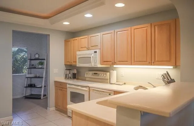 Kitchen featuring white appliances, light wood finish cabinets, light countertops, a peninsula, and recessed lighting