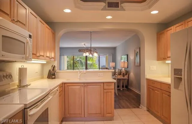 Kitchen featuring white appliances, light countertops, a peninsula, a chandelier, and light wood finish cabinets