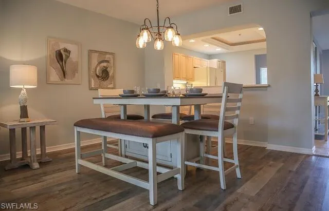 Dining room featuring dark wood-style flooring, a chandelier, a tray ceiling, and arched walkways