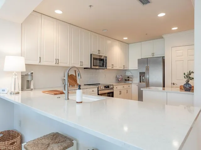 Kitchen featuring kitchen peninsula, a breakfast bar area, decorative backsplash, white cabinets, and appliances with stainless steel finishes