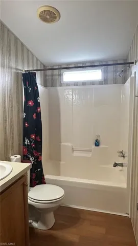Full bath featuring wallpapered walls, wood finished floors, vanity, and shower / tub combo