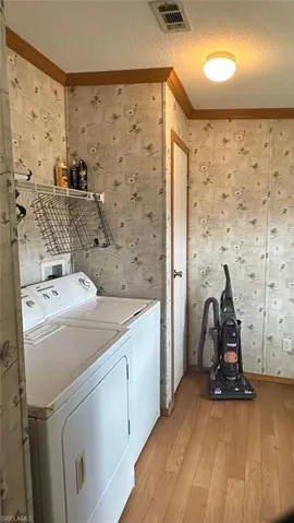 Washroom featuring wallpapered walls, washer and dryer, light wood-type flooring, and crown molding