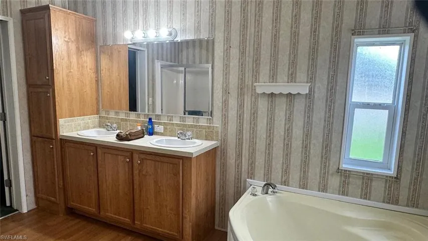 Bathroom featuring plenty of natural light, a garden tub, wood finished floors, double vanity, and wallpapered walls