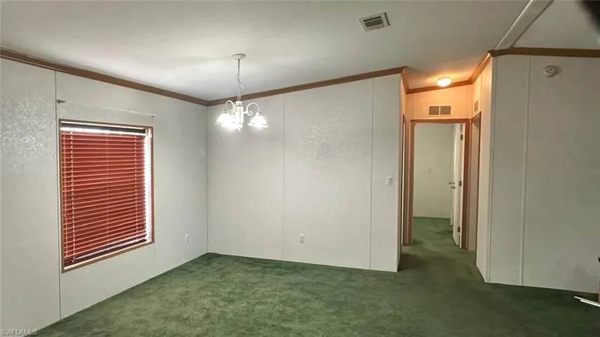 Unfurnished room featuring carpet, crown molding, and a chandelier