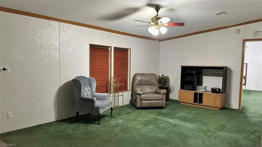 Living area featuring ceiling fan, carpet flooring, ornamental molding, and a textured wall