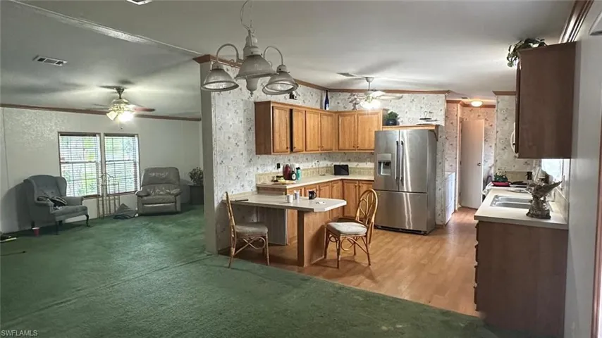 Kitchen with stainless steel fridge, a ceiling fan, a peninsula, crown molding, and light countertops