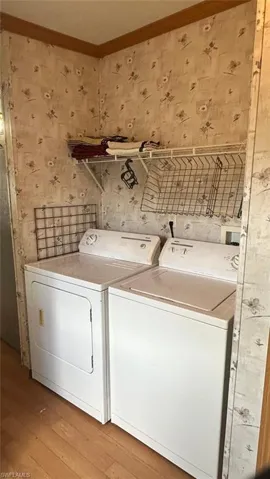 Laundry area with wallpapered walls, washer and clothes dryer, light wood-style floors, and ornamental molding