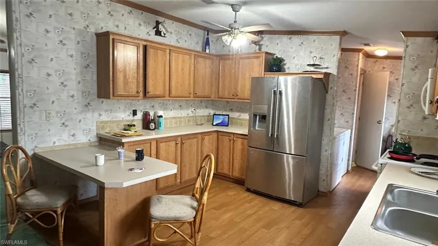 Kitchen featuring stainless steel fridge, wallpapered walls, light wood finished floors, a peninsula, and a breakfast bar area