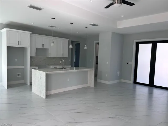 Kitchen with pendant lighting, white cabinets, sink, ceiling fan, and an island with sink