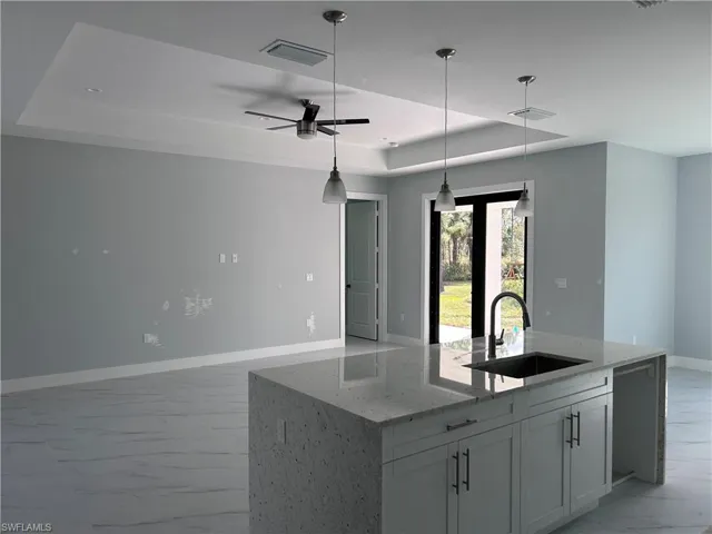 Kitchen featuring light stone counters, a tray ceiling, ceiling fan, sink, and a center island with sink
