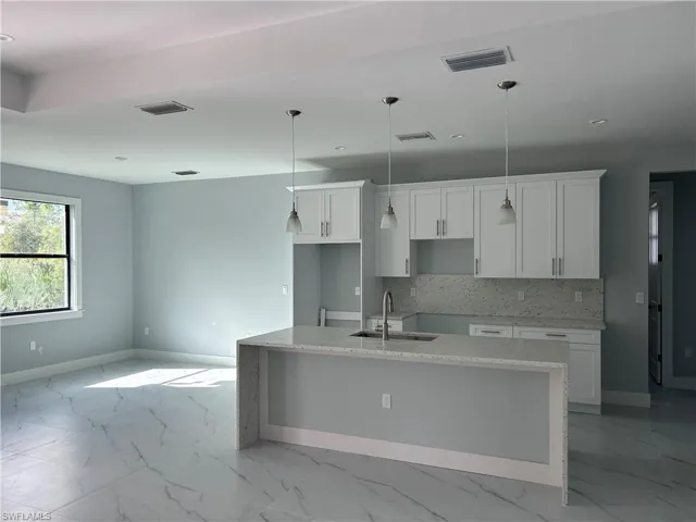 Kitchen with white cabinets, light stone counters, sink, and an island with sink