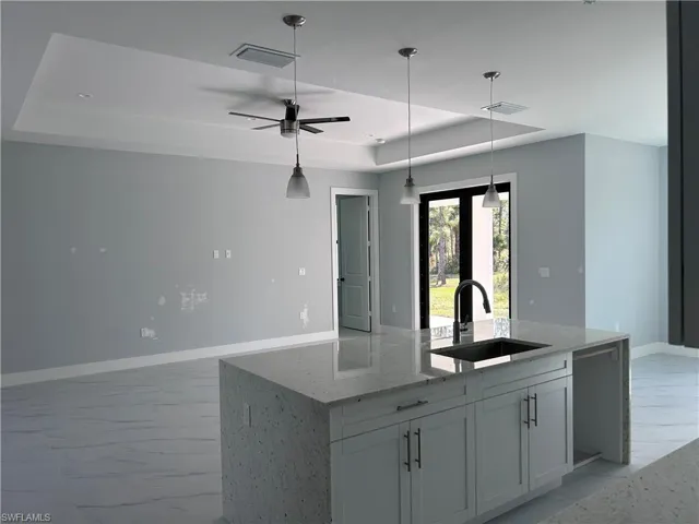 Kitchen featuring dishwasher, sink, ceiling fan, light stone counters, and white cabinetry