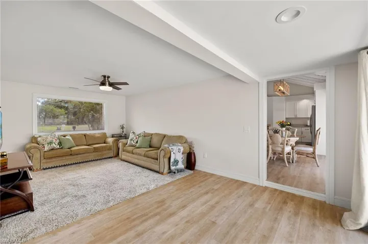 Living area with a ceiling fan, light wood-style flooring, baseboards, and beam ceiling