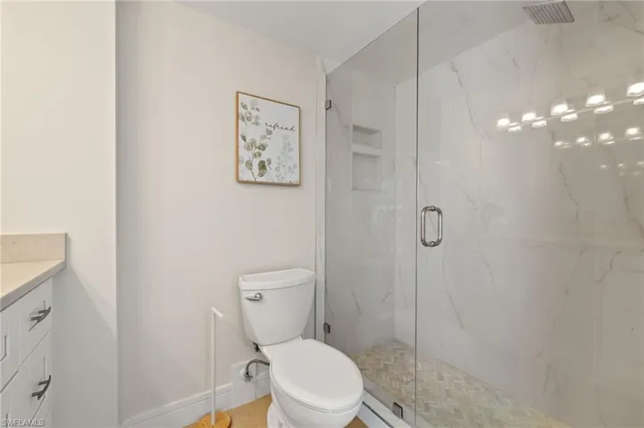 Bathroom featuring baseboards, toilet, vanity, and a marble finish shower