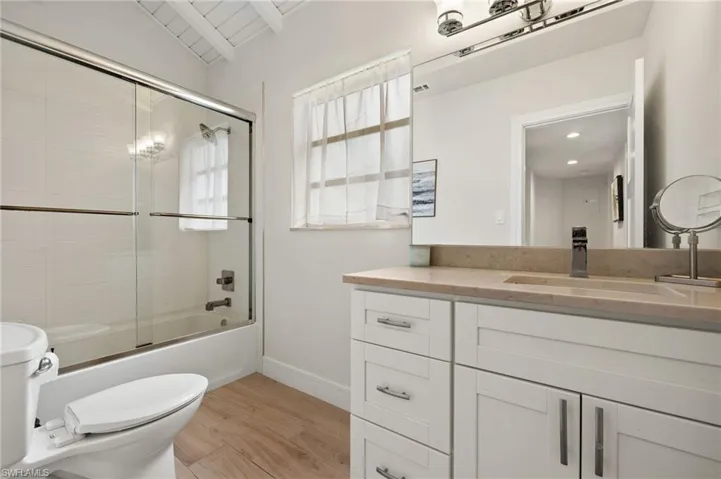 Full bathroom with enclosed tub / shower combo, toilet, wood finished floors, vanity, and baseboards