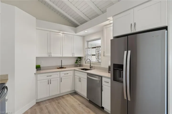 Kitchen featuring white cabinets, lofted ceiling with beams, appliances with stainless steel finishes, light countertops, and a sink