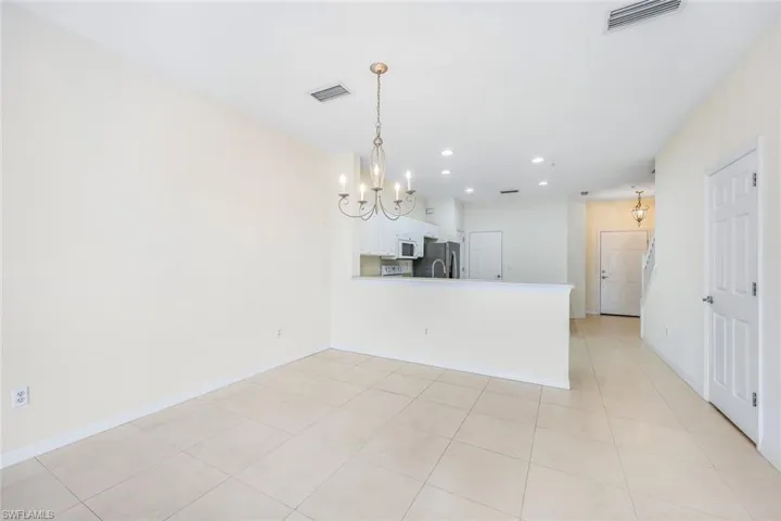 Kitchen featuring light tile patterned flooring, white cabinetry, a notable chandelier, kitchen peninsula, and stainless steel fridge