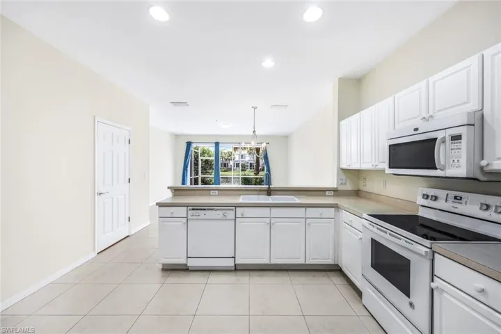 Kitchen with white appliances, light tile patterned floors, kitchen peninsula, hanging light fixtures, and sink