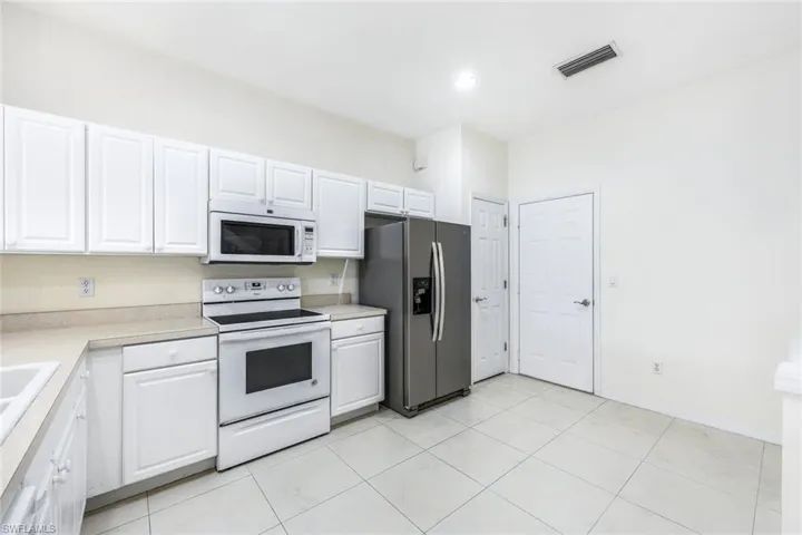 Kitchen with sink, light tile patterned floors, white cabinets, and white appliances