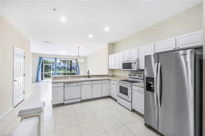 Kitchen featuring white appliances, white cabinets, kitchen peninsula, hanging light fixtures, and light tile patterned flooring