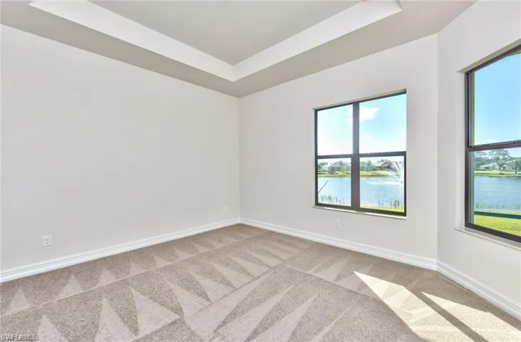 Carpeted bedroom featuring a tray ceiling, baseboards, and a water view
