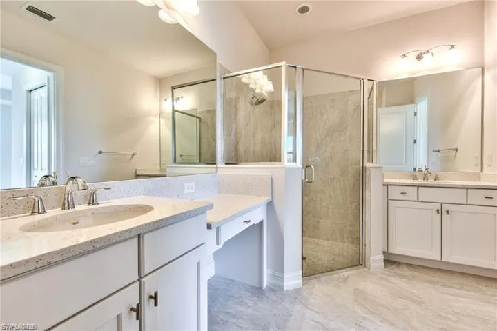Full bath with two vanities, visible vents, a stall shower, and a sink