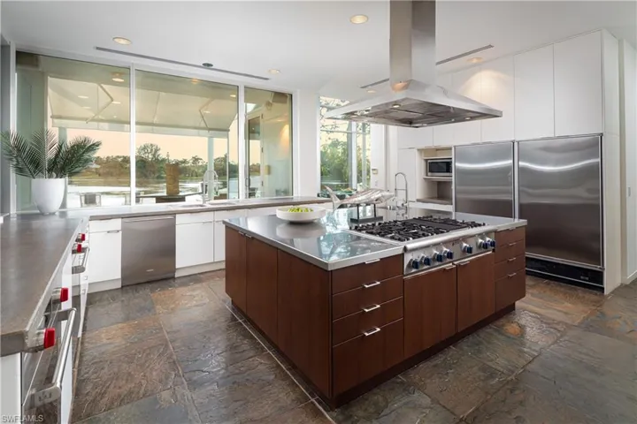 Kitchen featuring island exhaust hood, built in appliances, a healthy amount of sunlight, and a center island with sink