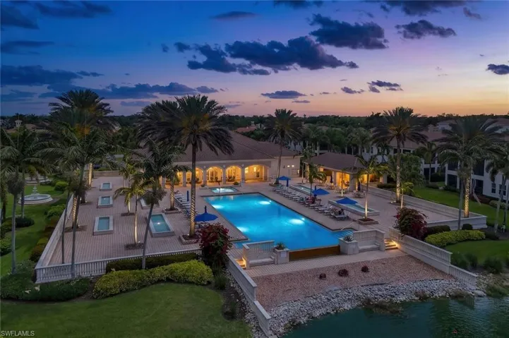 Expansive swimming pool and spa area featuring a paver deck, mature palm trees, decorative water features, and a waterside promenade