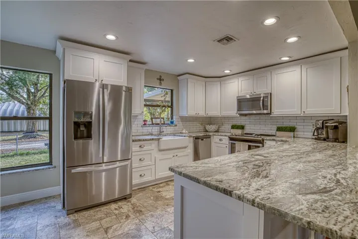Kitchen featuring stainless steel appliances, white cabinets, light stone counters, tasteful backsplash, and recessed lighting