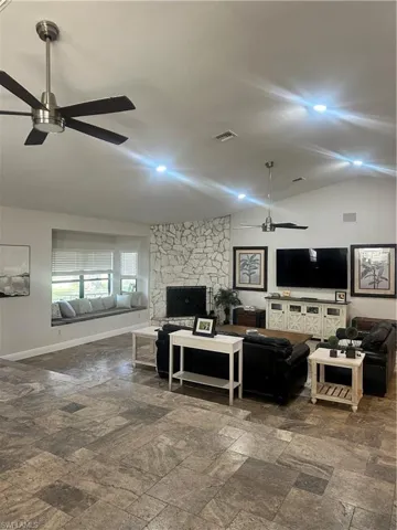 Living room with ceiling fan, lofted ceiling, stone tile floors, and a fireplace