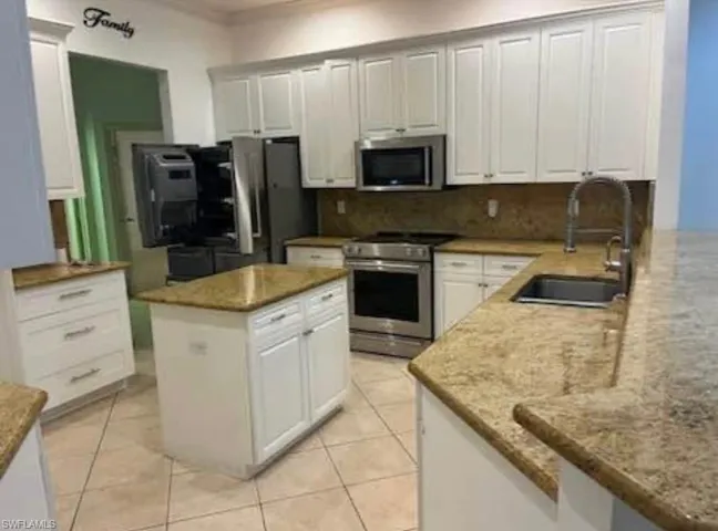Kitchen with white cabinets, appliances with stainless steel finishes, light stone counters, a center island, and light tile patterned floors