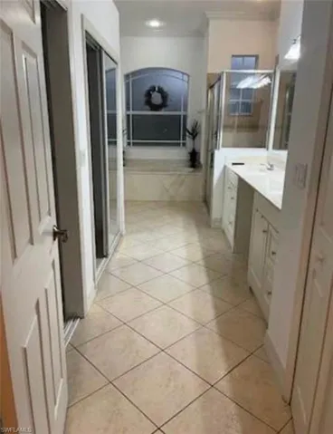 Bathroom featuring a stall shower, vanity, a garden tub, light tile patterned floors, and crown molding