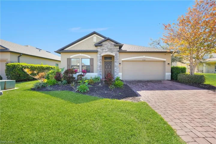 View of front of home featuring driveway, a front yard, stone siding, stucco siding, and a garage