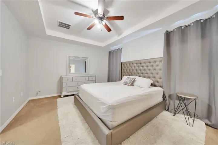 Bedroom featuring a tray ceiling, a ceiling fan, baseboards, light colored carpet, and visible vents